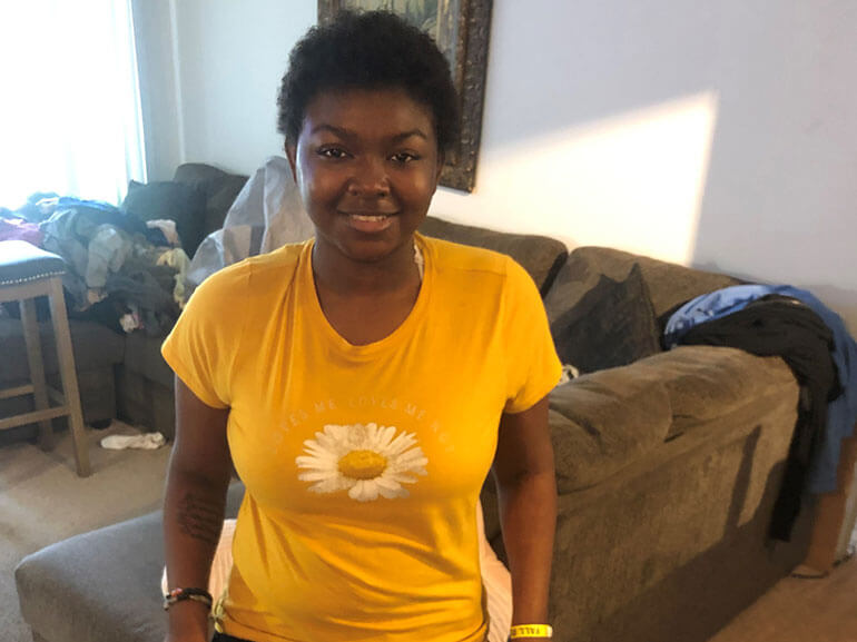 Amirah Williams smiling in living room wearing a yellow t-shirt.